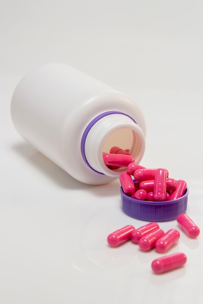 Close-up of an open white bottle with pink capsules spilled onto the surface.