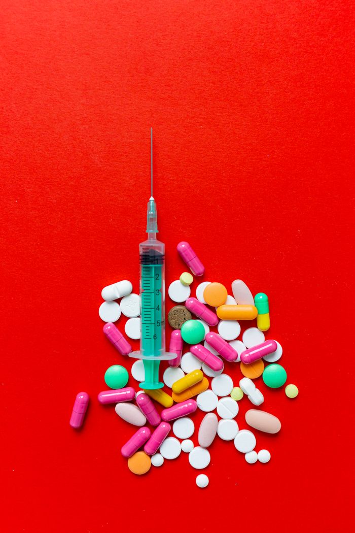 Colorful assortment of pills and a syringe on a vibrant red background, representing medication and healthcare.